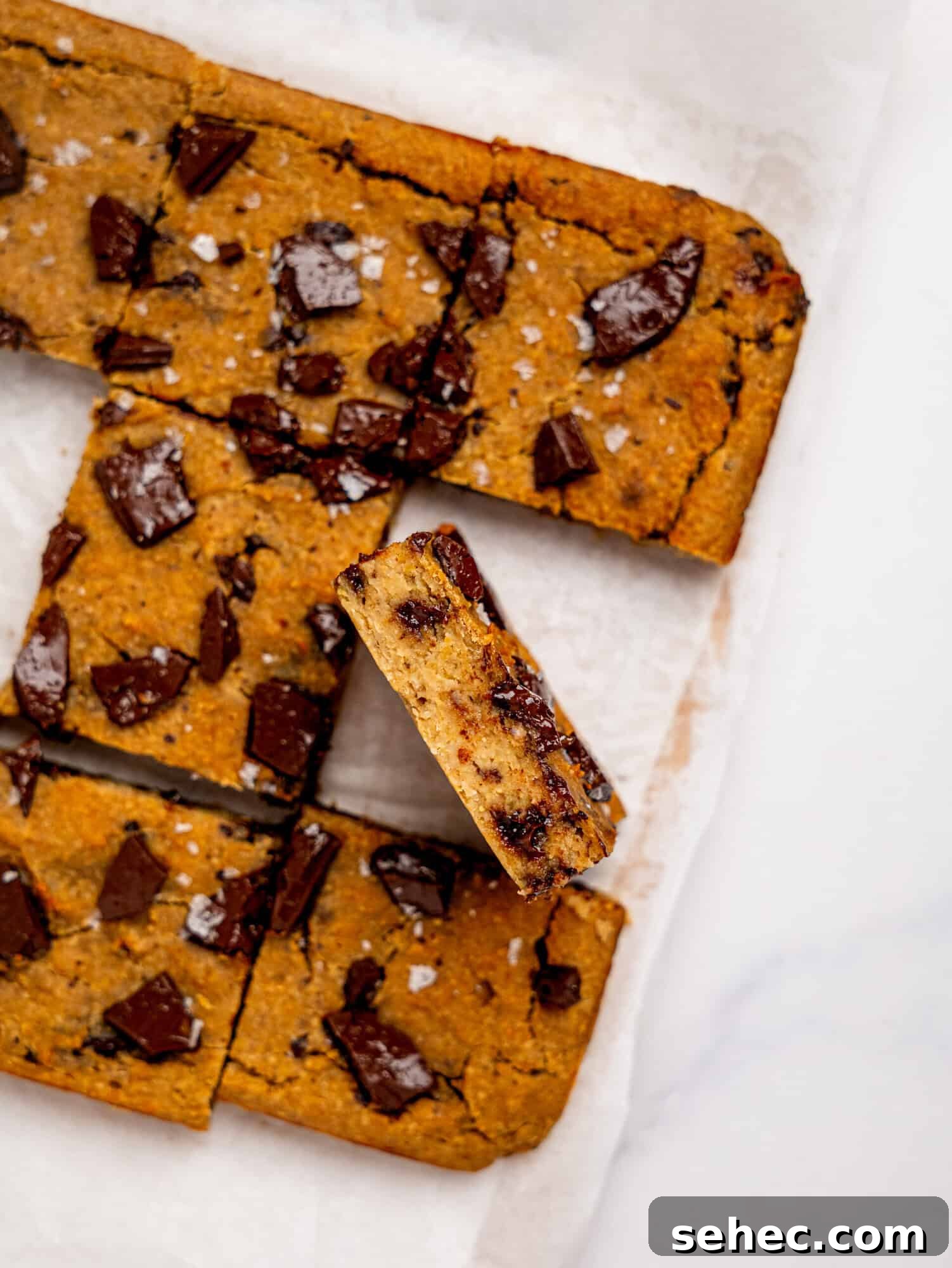 Gooey Chickpea Cookie Bars 6 Bird's eye view of chickpea cookie bars on a sheet of white parchment paper, one is turned on its side to reveal the fudgy texture.