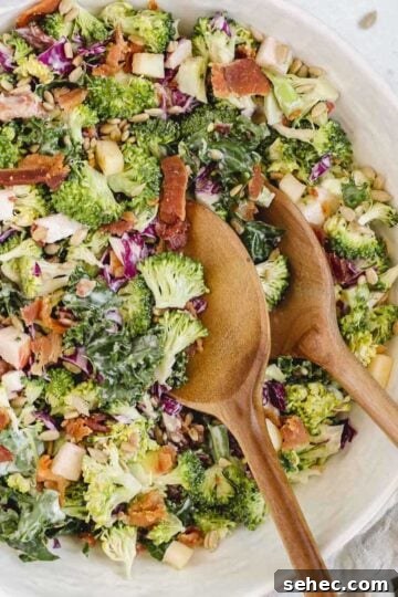Broccoli salad with kale and red cabbage in a large serving bowl with wooden salad utensils in the bowl.