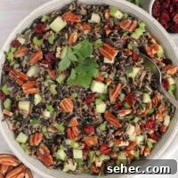 Cold Wild Rice Salad with Cranberries and Pecans 15 Wild rice salad with pecans, dried cranberries, and apples in a ceramic serving bowl with a vintage serving spoon in the salad.