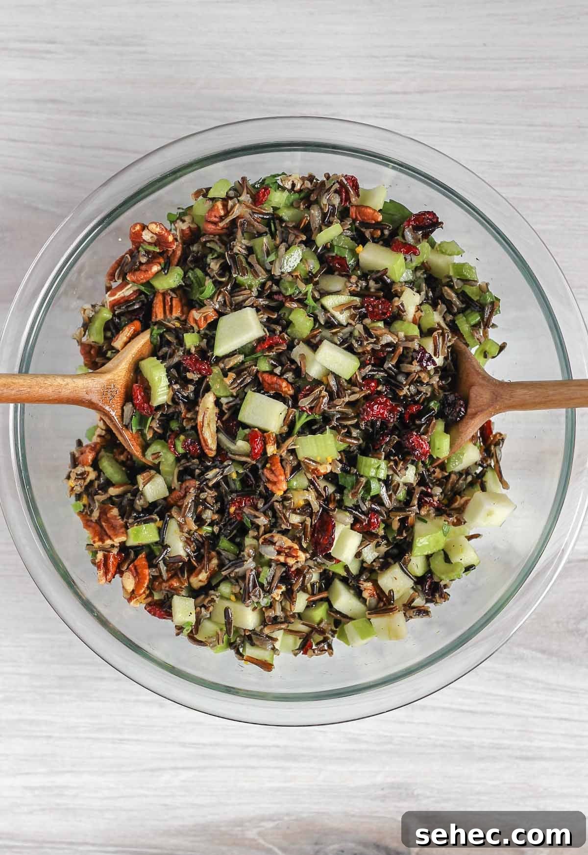 Cold Wild Rice Salad with Cranberries and Pecans 9 Two wooden salad utensils mixing wild rice salad ingredients in a glass mixing bowl.