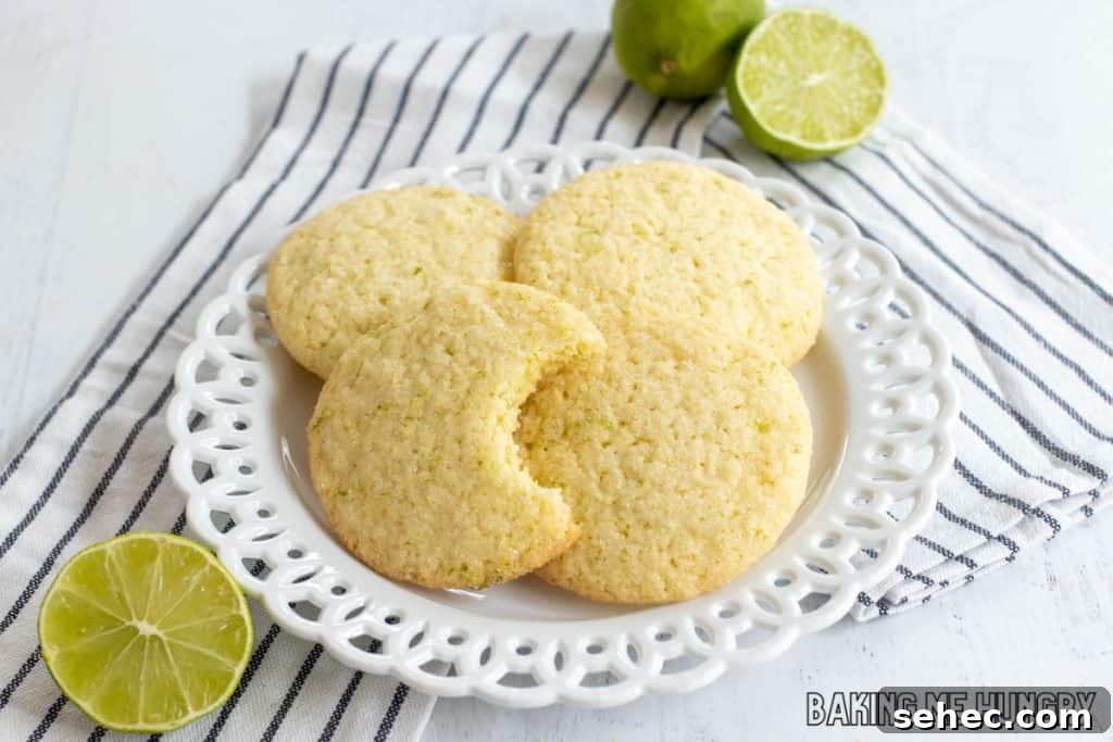 Soft Lime Sugar Cookies with Zesty Citrus Glaze 11 lime sugar cookies on a plate on a striped napkin with one missing a bite