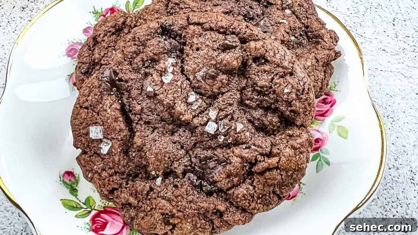 17 Buttery Fall Cookie Recipes for Cozy Shorter Days 16 A close-up of a large chocolate cookie sprinkled with coarse salt, placed on a decorative plate with pink rose patterns.