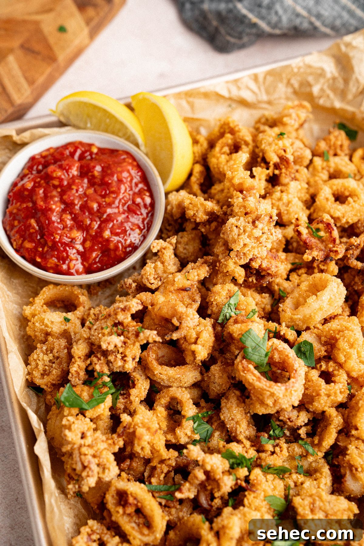 Crispy Fried Calamari with Tender Squid Rings 6 Fried calamari on a pan for serving with a small bowl of marinara sauce and lemon wedges.