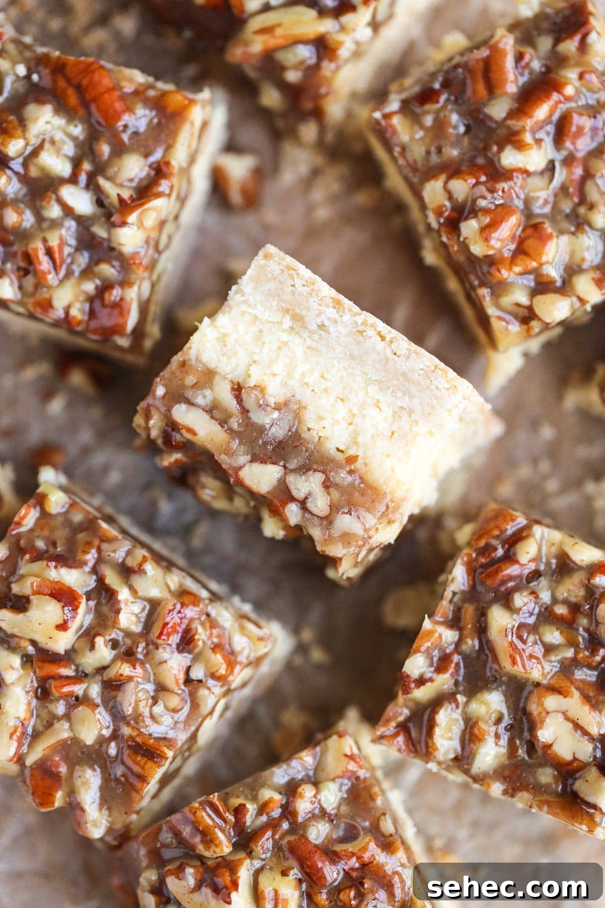 Pecan Pie Cheesecake Bars Recipe 2 pecan pie cheesecake bars on parchment paper.