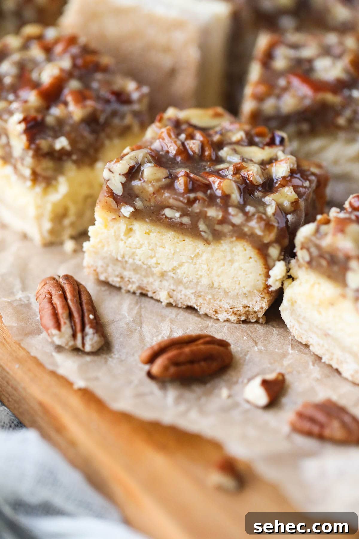 Pecan Pie Cheesecake Bars Recipe 3 pecan pie cheesecake bars on parchment paper.