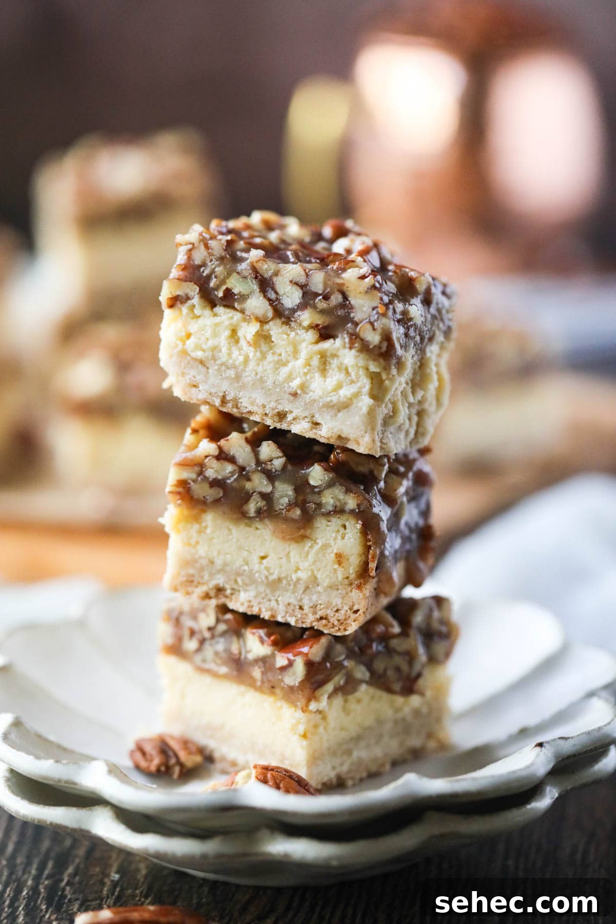 Pecan Pie Cheesecake Bars Recipe 7 pecan pie cheesecake bars stacked on a white plate.