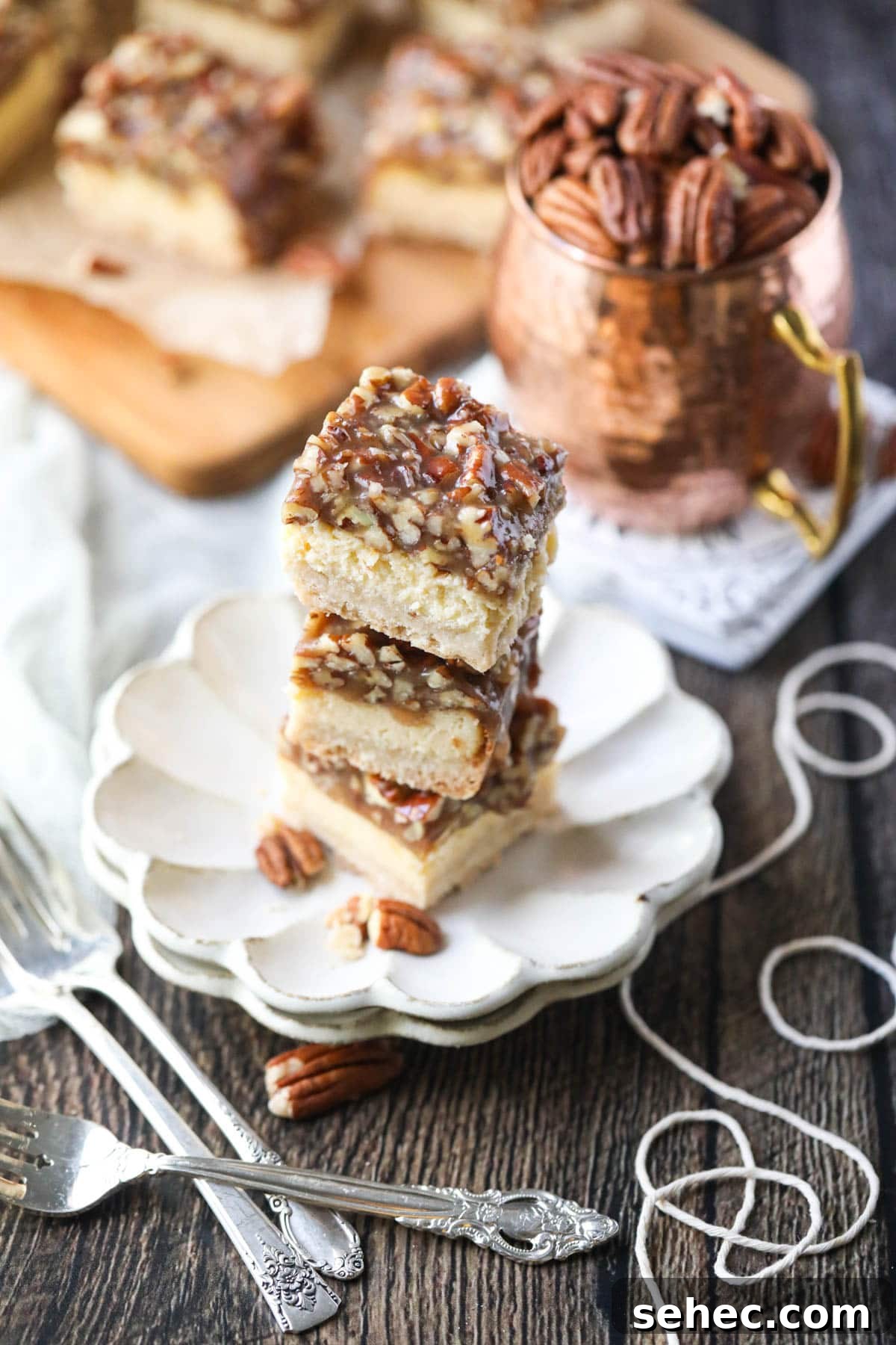 Pecan Pie Cheesecake Bars Recipe 9 pecan pie cheesecake bars stacked on a white plate.
