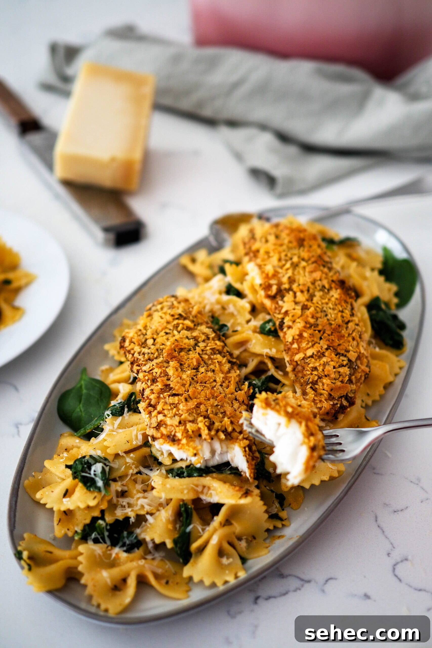 Cajun Tortilla Chip Crusted Tilapia Recipe 2 Two breaded tilapia filets on top of a pile of Cajun pasta and spinach.