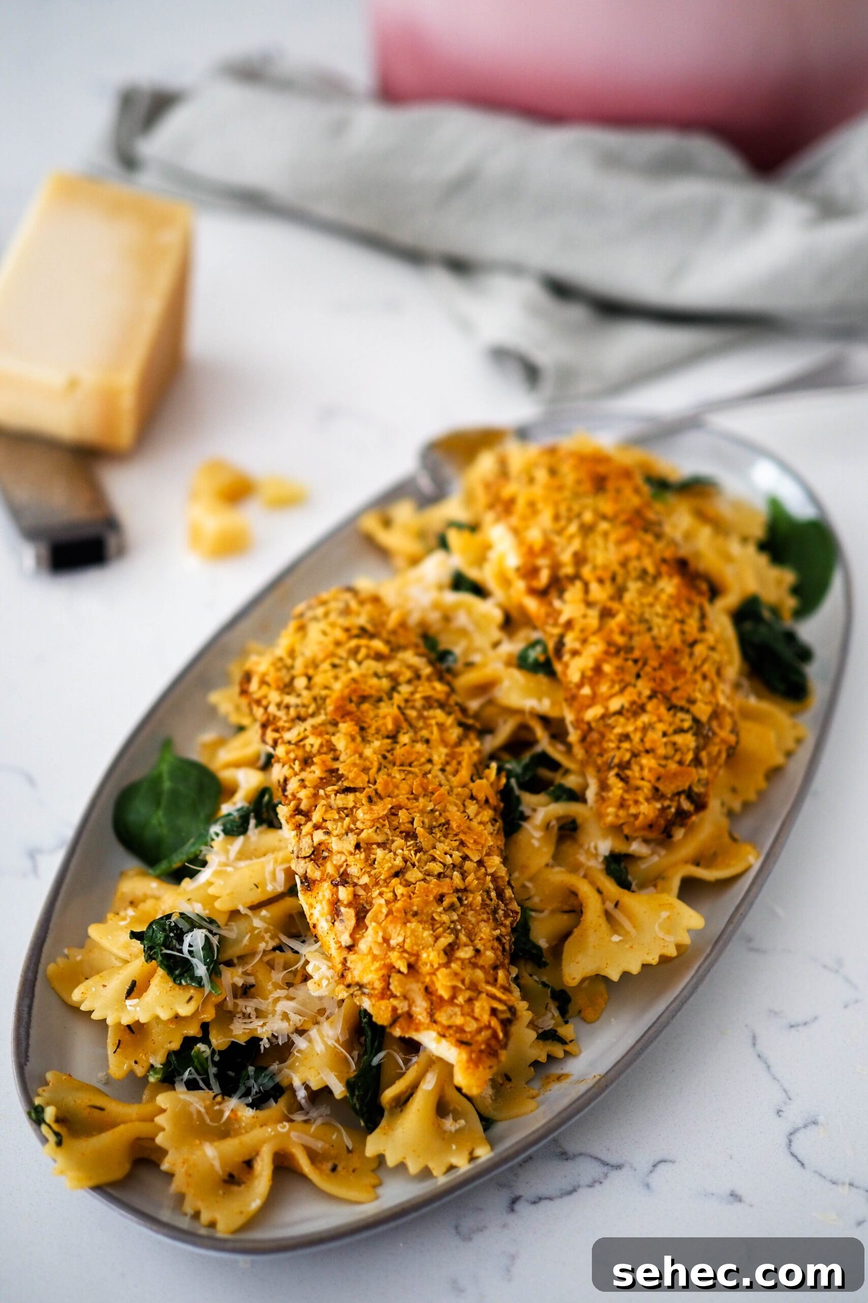 Cajun Tortilla Chip Crusted Tilapia Recipe 6 Two breaded tilapia filets on top of a pile of Cajun pasta and spinach.