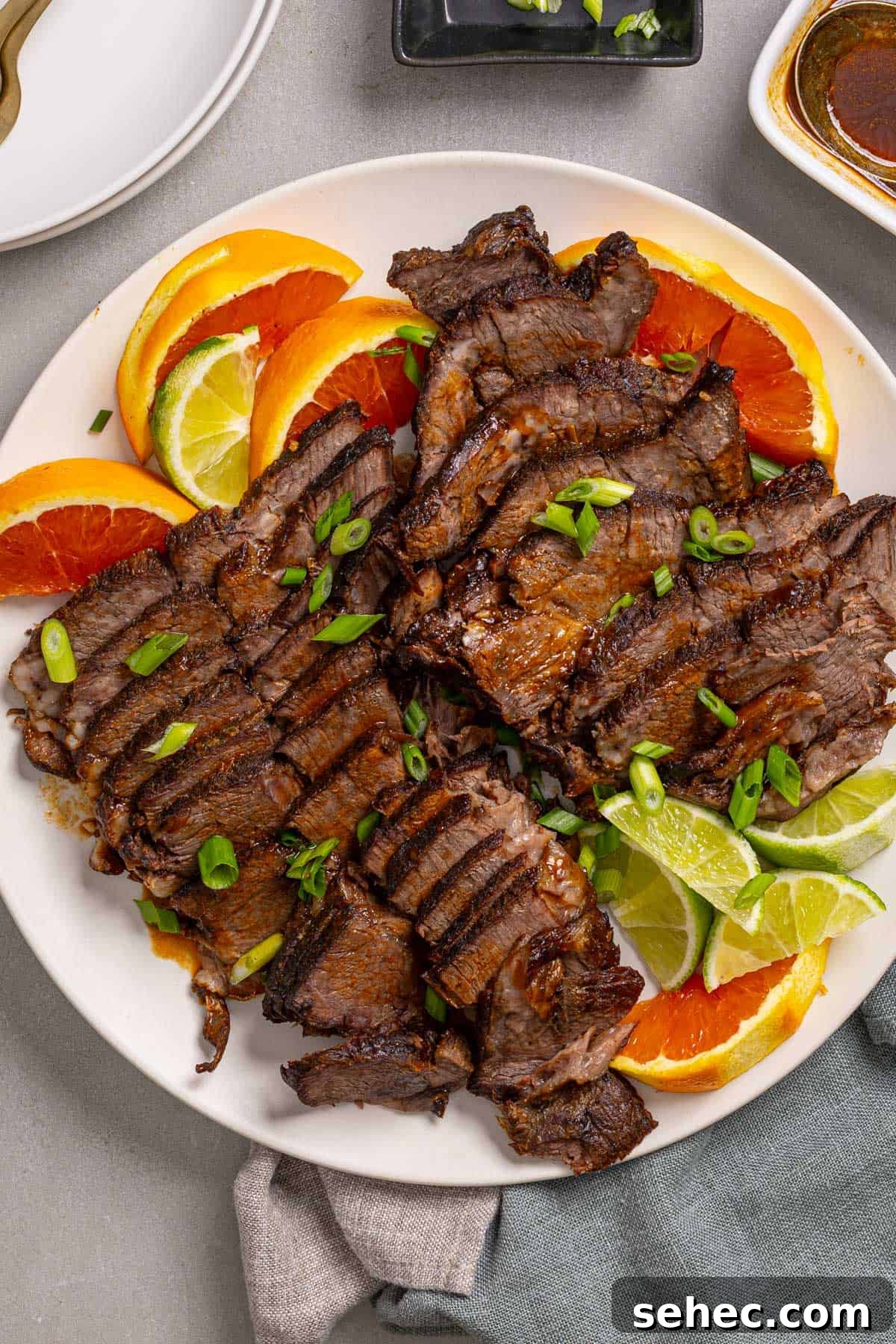 Citrus Soy Braised Chuck Roast Recipe 2 A close up of a platter with braised chuck roast sliced thin garnished with orange and lime.