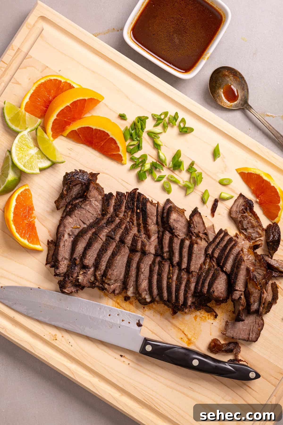 Citrus Soy Braised Chuck Roast Recipe 8 A cutting board with sliced of orange and lime, scallions, and braised chuck roast.