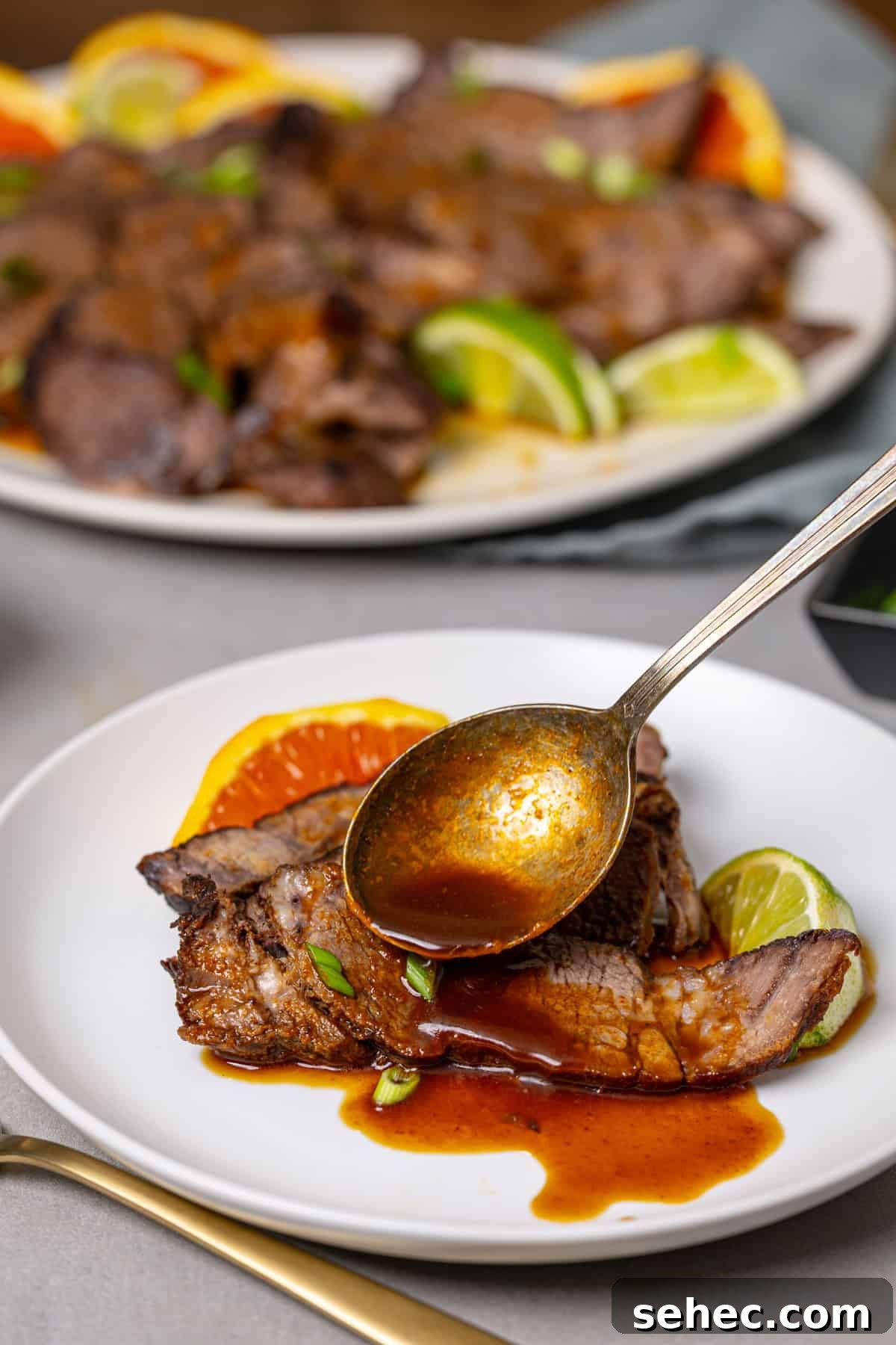 Citrus Soy Braised Chuck Roast Recipe 9 A close up of a plate of braised chuck roast with a spoon topping it with a brown sauce.