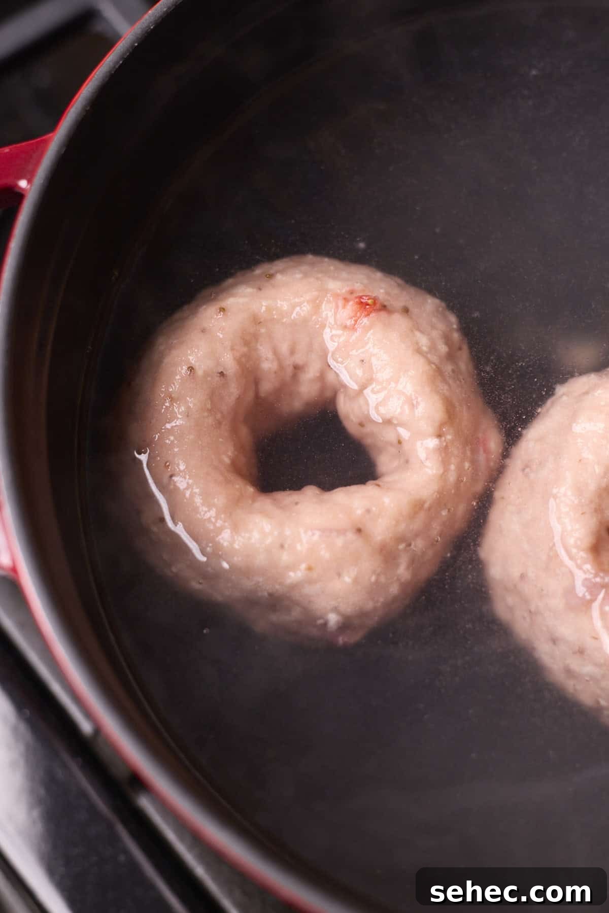 Strawberry Sourdough Discard Bagels 11 Bagels boiling in a pot of water.