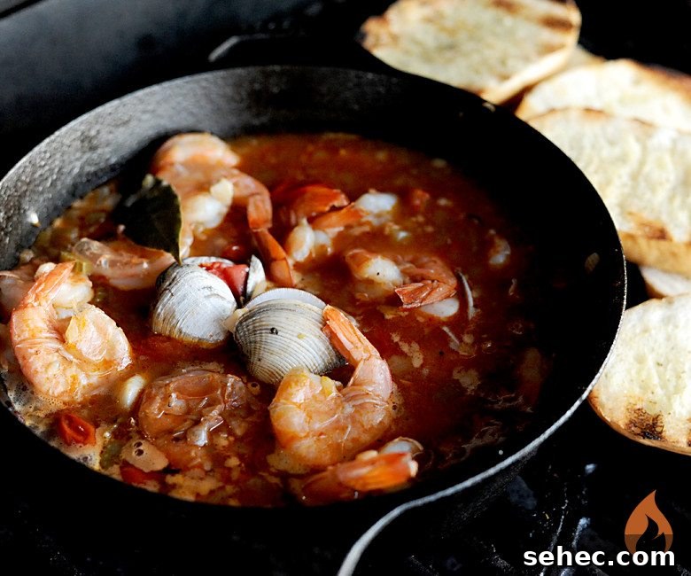 cast iron pot of grilled cioppino with toasted bread