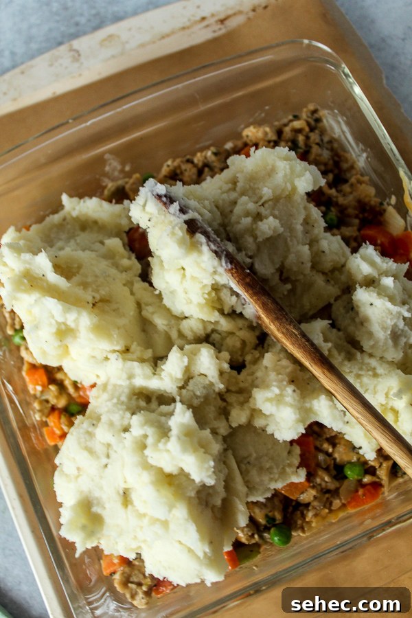 Ground Turkey Shepherds Pie Recipe 5 A large wooden spoon spreading fresh, fluffy mashed potatoes over shepherd's pie.
