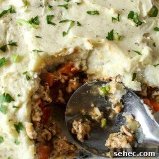 Ground Turkey Shepherds Pie Recipe 8 a glass dish with shepherds pie topped with parsley and a large silver spoon in the dish