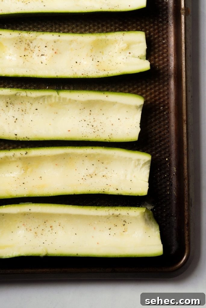 Buffalo Chicken Zucchini Boats Recipe 6 scooped out zucchinis on a baking sheet seasoned with salt and pepper