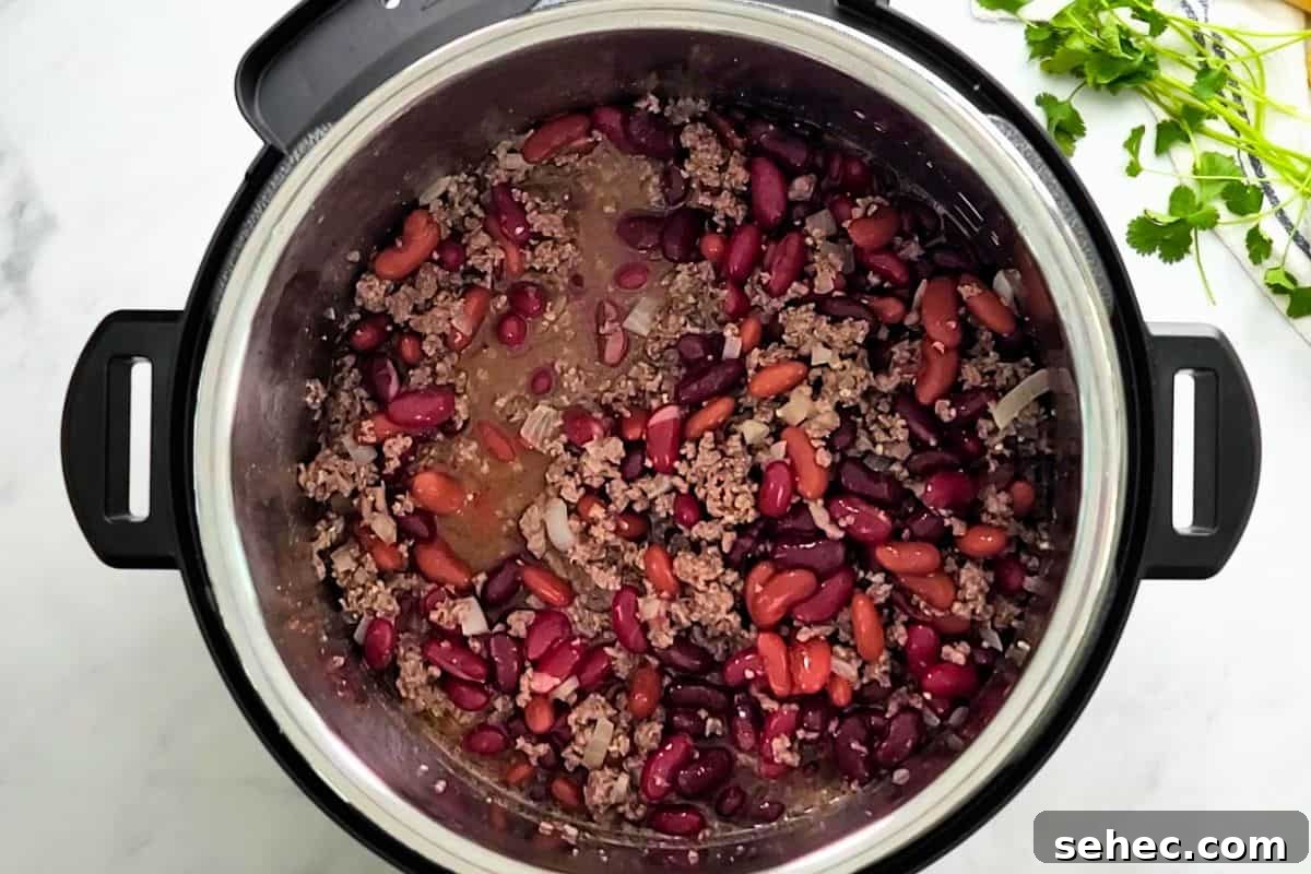 Instant Pot Chili Recipe Sauteed beef with beer, beef stock, and kidney beans mixed together inside Instant Pot.
