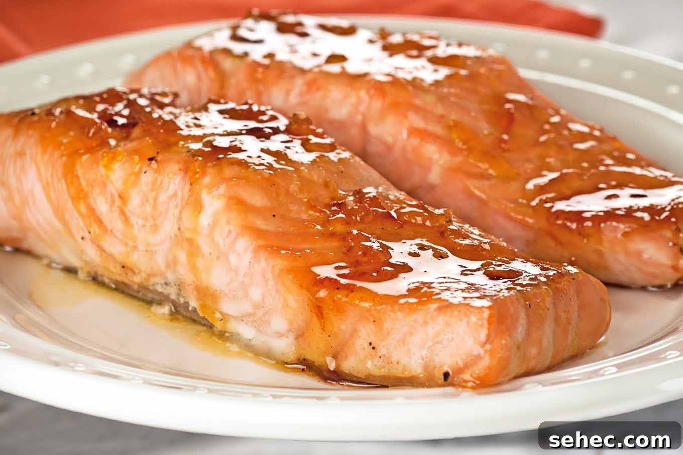 Bourbon Orange Marmalade Glazed Salmon Recipe 3 Close-up of two orange marmalade and bourbon glazed salmon on a white serving plate.