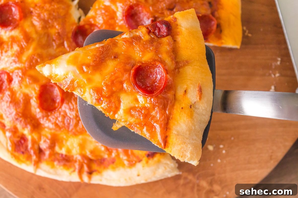 Crispy Chewy Sourdough Pizza Crust Recipe 2 A slice of homemade pepperoni pizza made with sourdough pizza crust sitting on a spatula