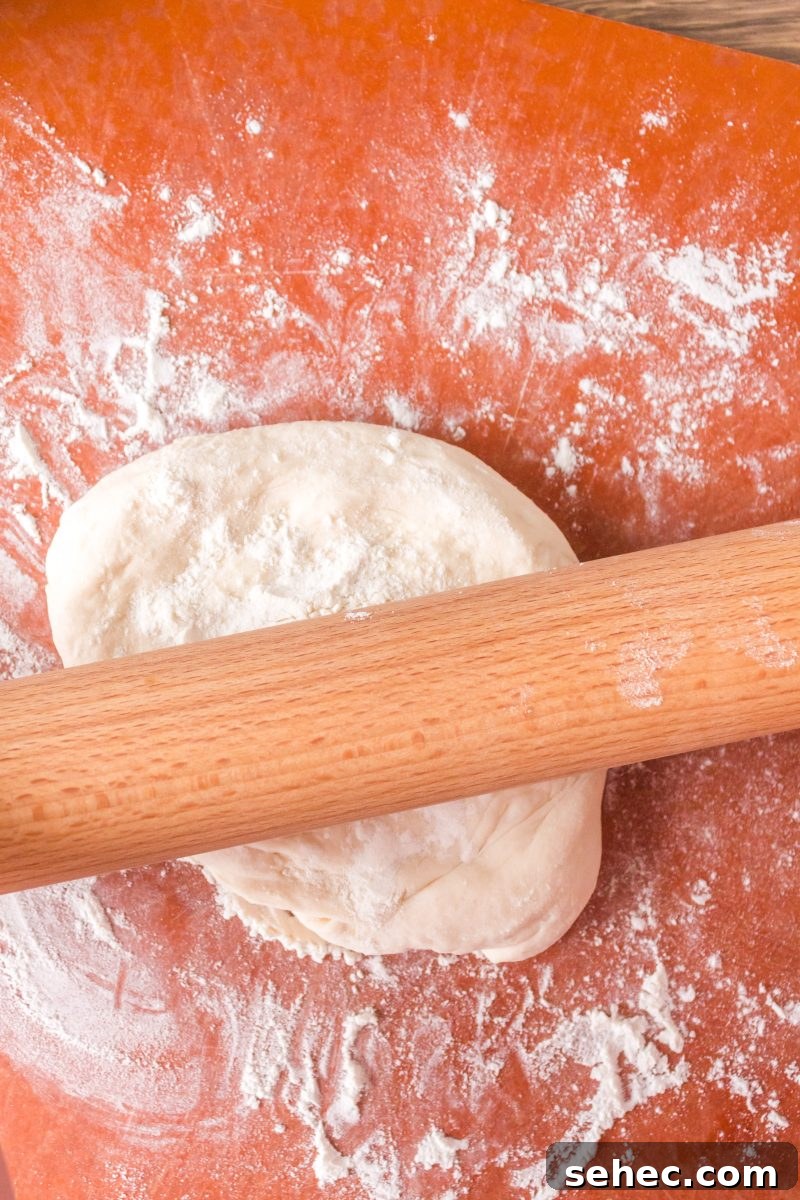 Crispy Chewy Sourdough Pizza Crust Recipe 12 A rolling pin rolling homemade pizza crust on a floured surface