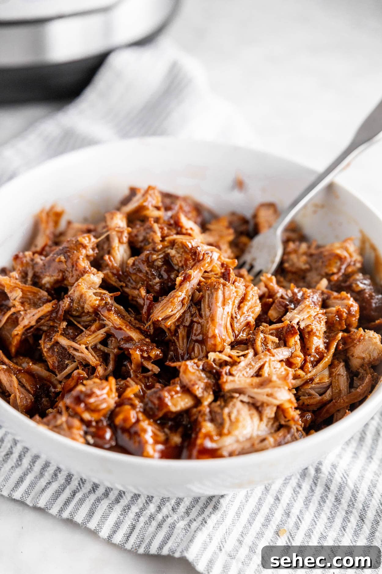 Instant Pot BBQ Pulled Pork Recipe 3 A photo of a large bowl with shredded BBQ pulled pork and a fork.