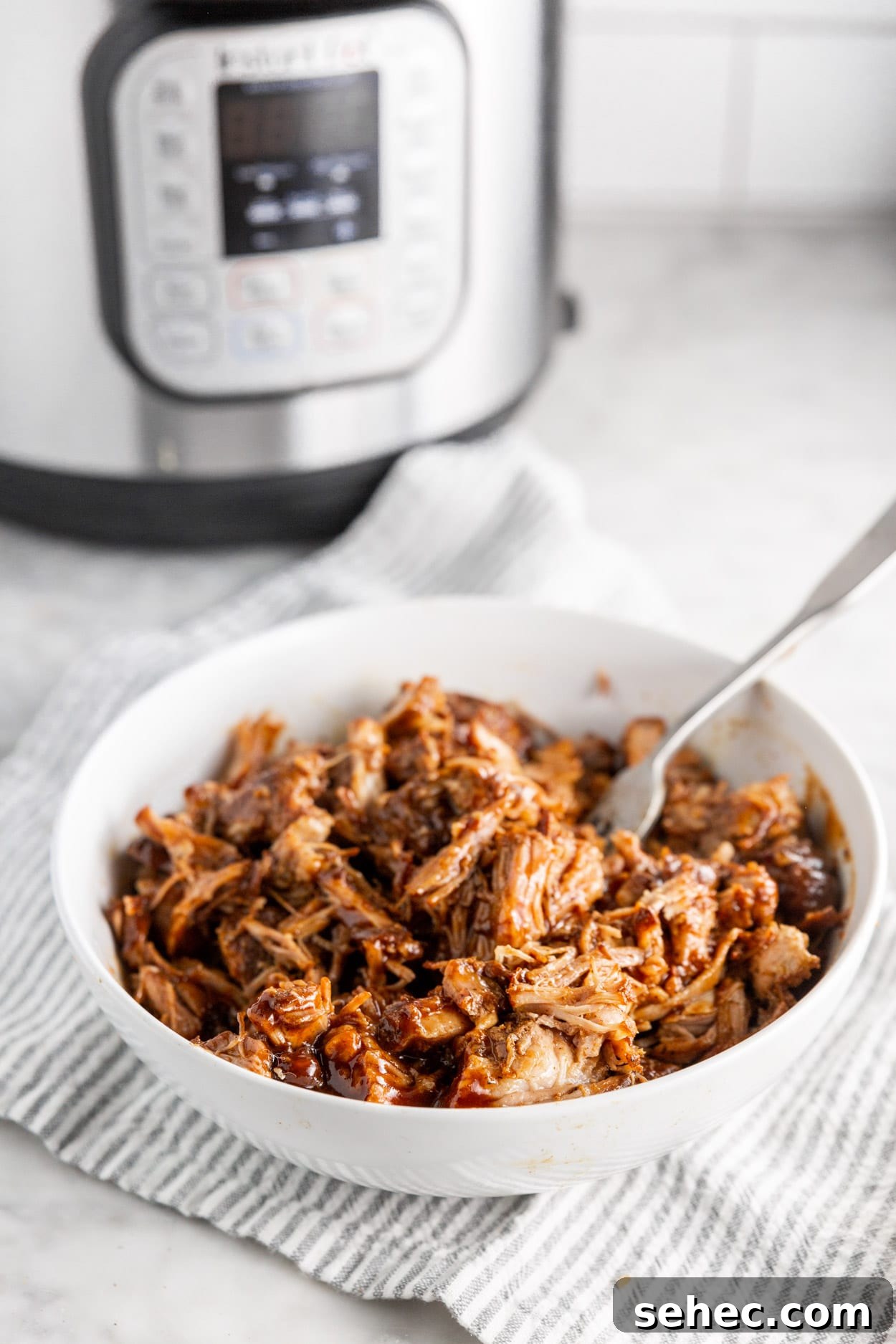 Instant Pot BBQ Pulled Pork Recipe 6 A bowl of shredded BBQ pulled pork in a bowl with an Instant Pot in the background.