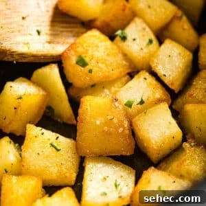 Crispy Fried Potatoes Recipe 13 A close up of fried potatoes in a pan with a wooden spoon in it.