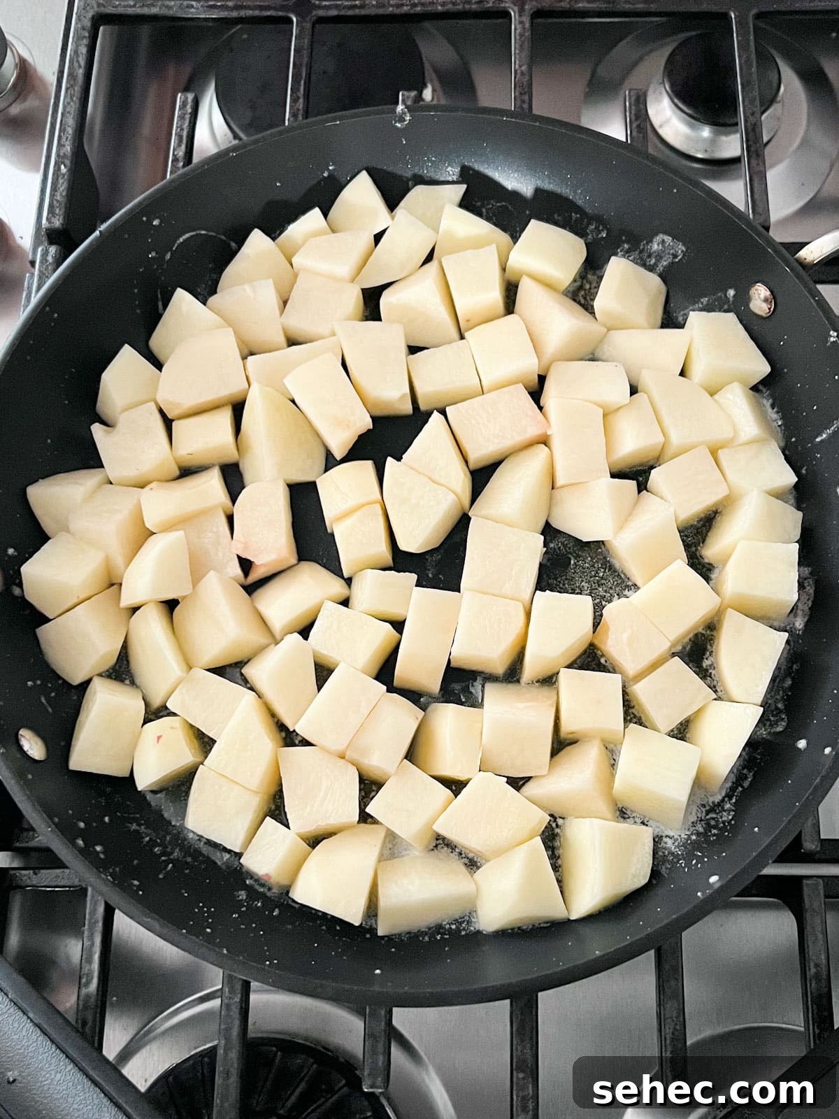 Crispy Fried Potatoes Recipe 5 Raw potatoes cooking in a pan.