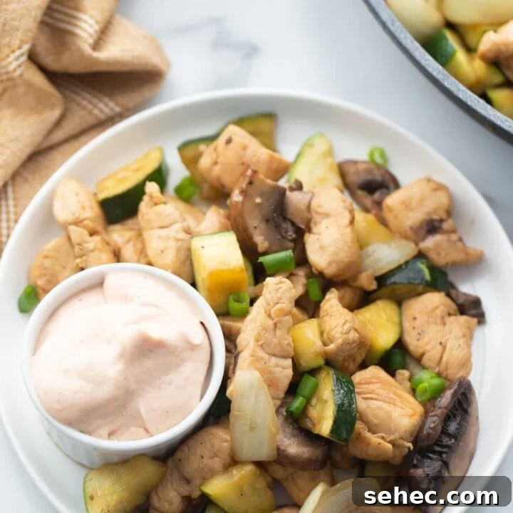 A plate is presented with chicken, veggies, and a small cup of yum yum sauce.