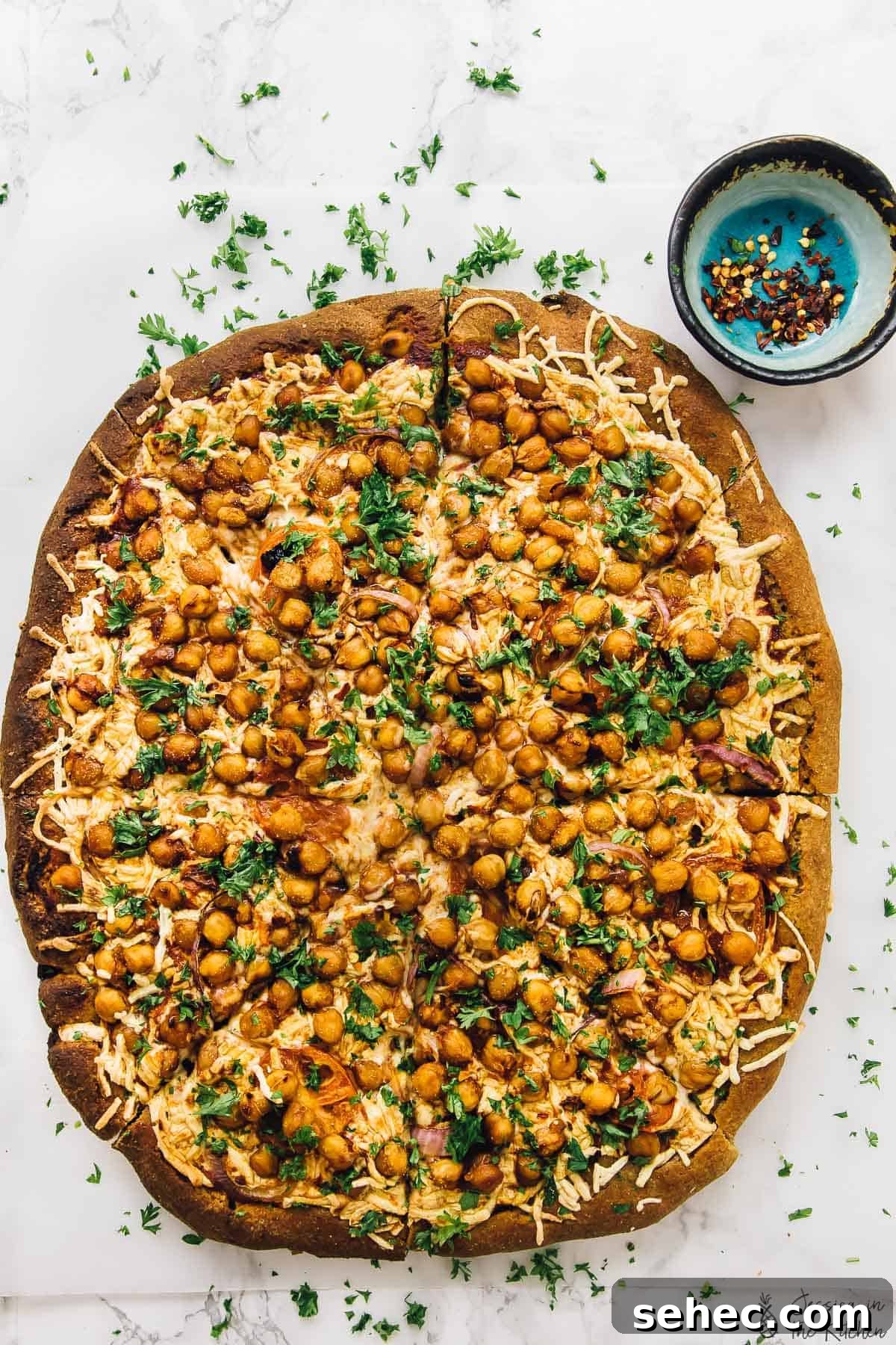 Spicy BBQ chickpea pizza is like a vegan version of BBQ chicken pizza, with a bit of a kick. An easy plant-based dinner ready in a flash! Overhead view of sliced BBQ chickpea pizza on parchment-lined baking sheet with parsley for garnish