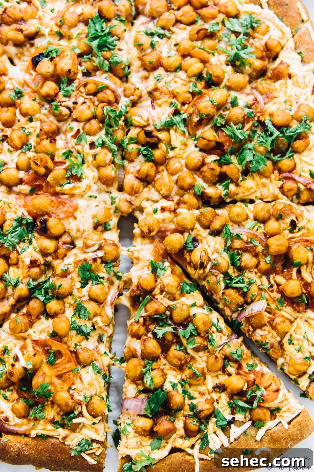 Spicy BBQ chickpea pizza is like a vegan version of BBQ chicken pizza, with a bit of a kick. An easy plant-based dinner ready in a flash! Overhead view of whole spicy BBQ chickpea pizza with one slice pulled away slightly