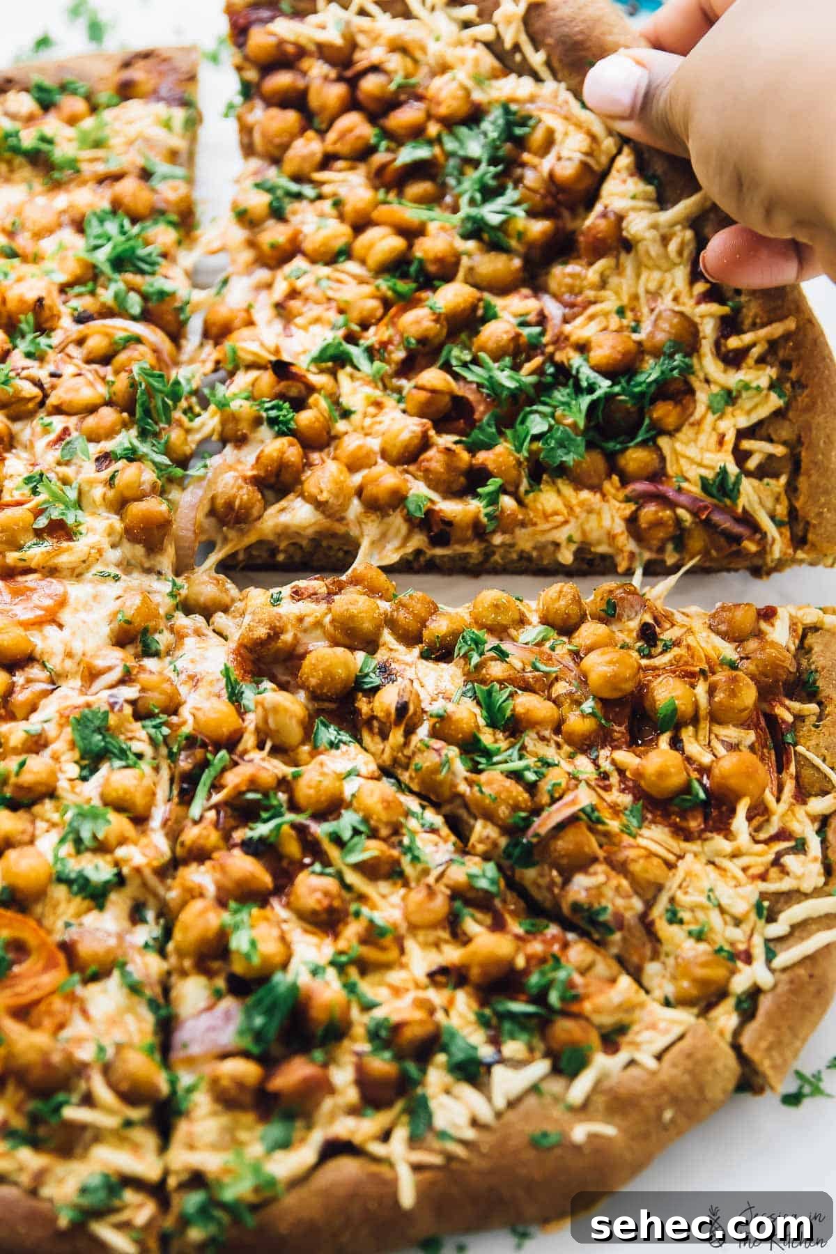 Spicy BBQ chickpea pizza is like a vegan version of BBQ chicken pizza, with a bit of a kick. An easy plant-based dinner ready in a flash! Hand pulling away slice of spicy BBQ chickpea pizza
