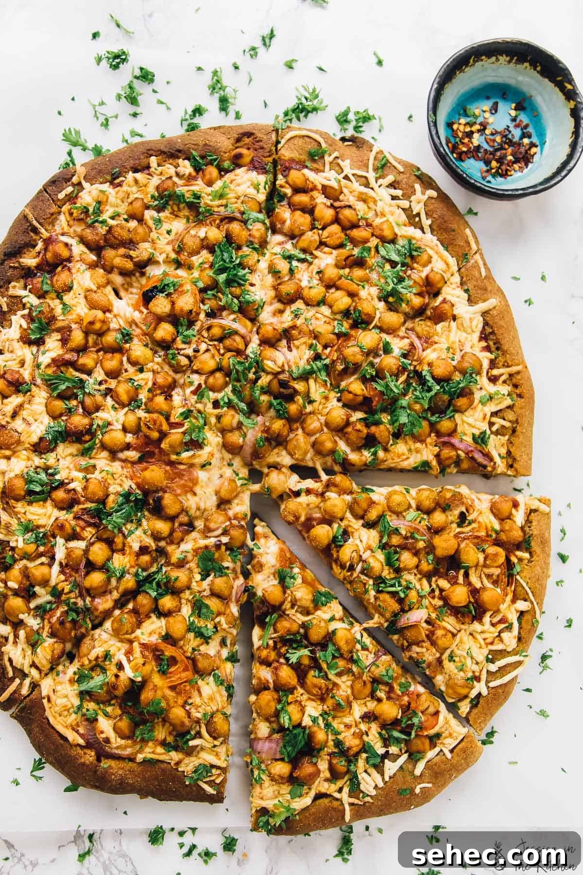 Spicy BBQ chickpea pizza is like a vegan version of BBQ chicken pizza, with a bit of a kick. An easy plant-based dinner ready in a flash! Overhead view of whole spicy BBQ chickpea pizza with two slices pulled away slightly