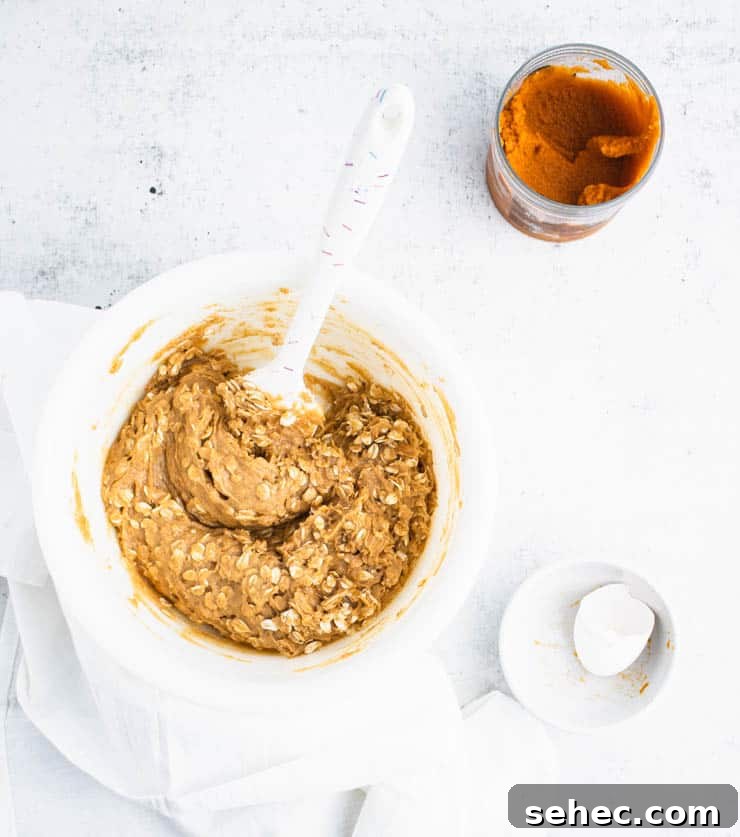 Pumpkin Oatmeal Cookies with Brown Butter Icing 3 pumpkin cookie batter with visible bits of rolled oats in a white bowl next to a bowl with egg shells and a container of pumpkin puree.