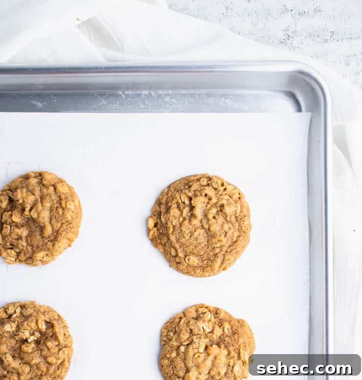 Pumpkin Oatmeal Cookies with Brown Butter Icing 4 baked pumpkin oatmeal cookies on parchment paper on a silver baking sheet.