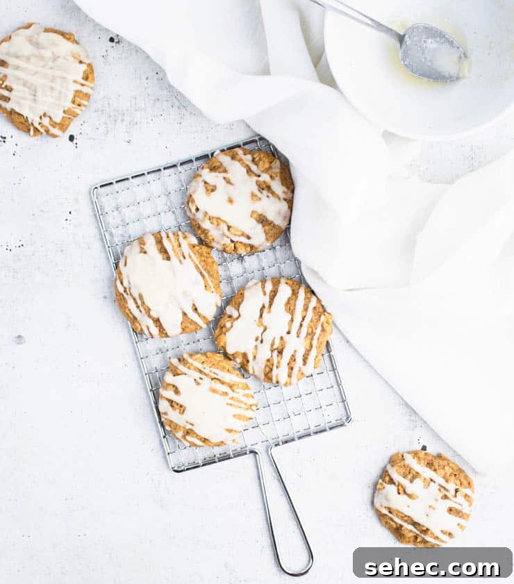 Pumpkin Oatmeal Cookies with Brown Butter Icing 6 brown butter iced pumpkin cookies on a small silver cooling rack next to a piece of white linen and a bowl.