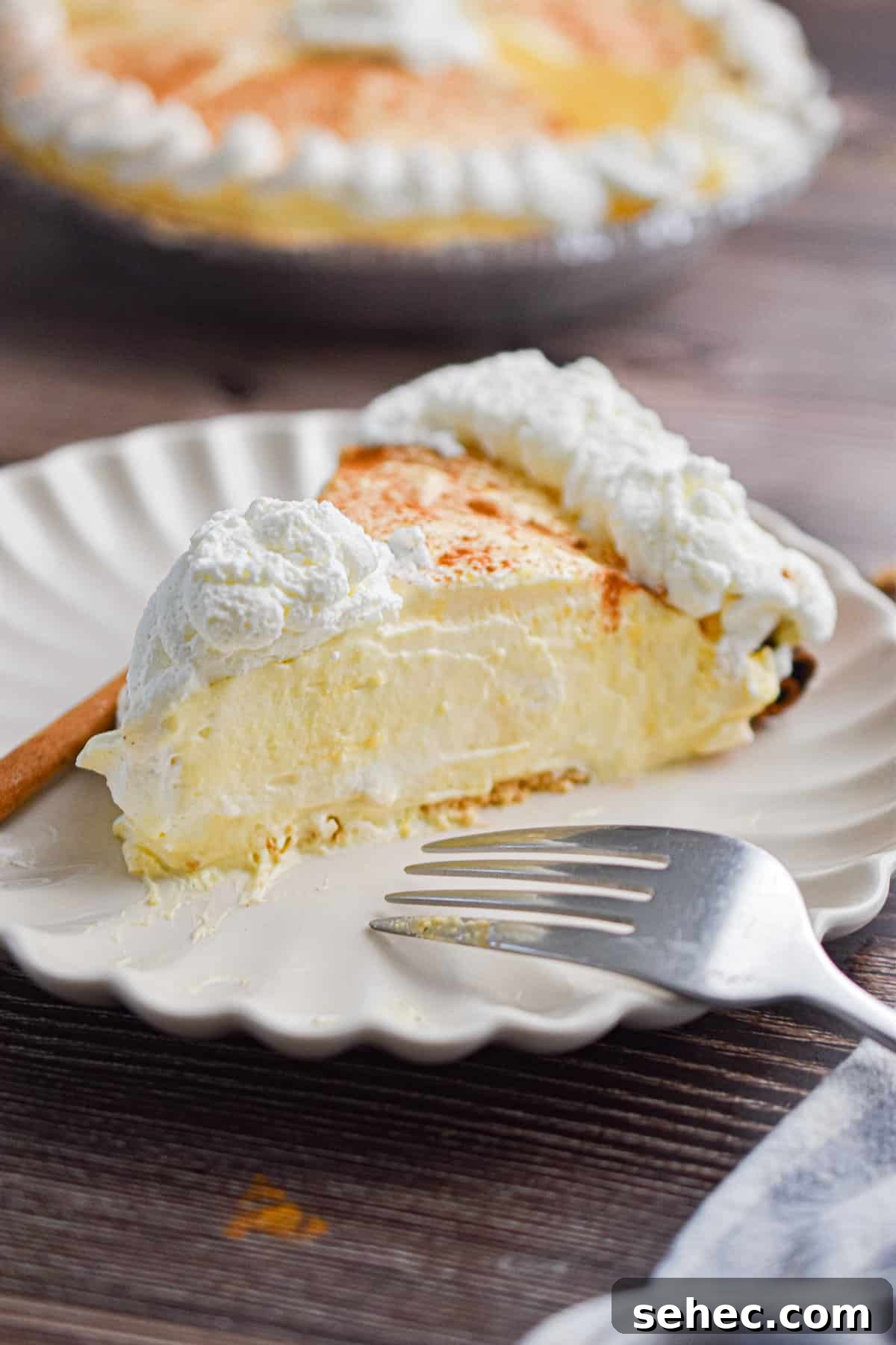 Eggnog Cream Pie Recipe for the Holidays 2 A slice of the no-bake eggnog pie is on a plate with a fork and a cinnamon stick.