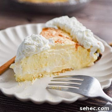 Eggnog Cream Pie Recipe for the Holidays 15 A slice of the no-bake eggnog pie is on a plate with a fork and a cinnamon stick.
