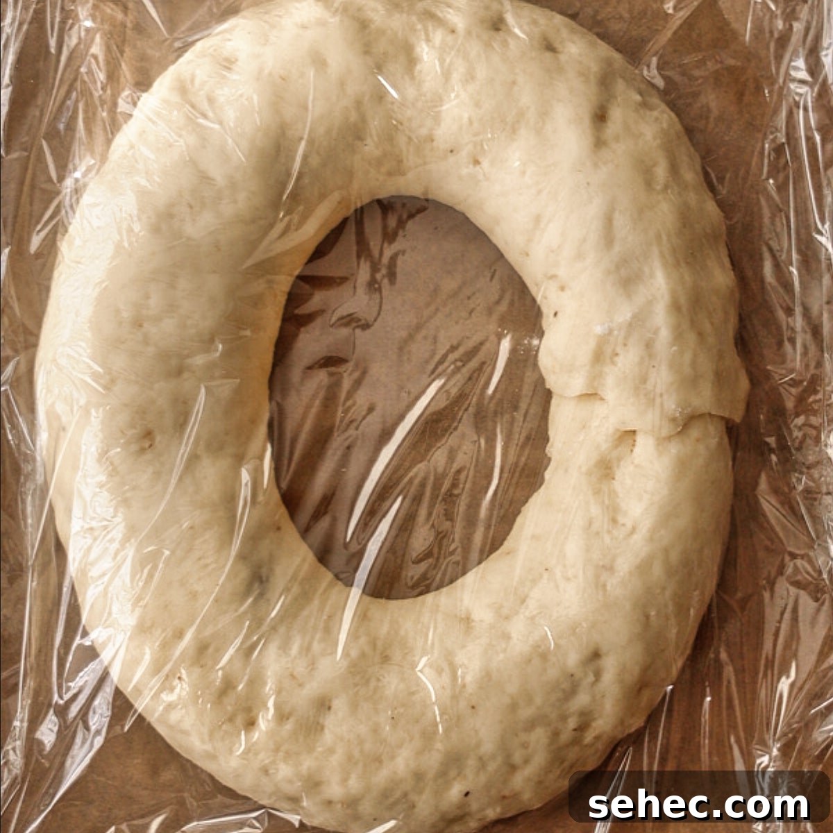 Gluten Free King Cake Recipe for Mardi Gras 14 king cake on parchment-lined baking sheet covered with plastic wrap.