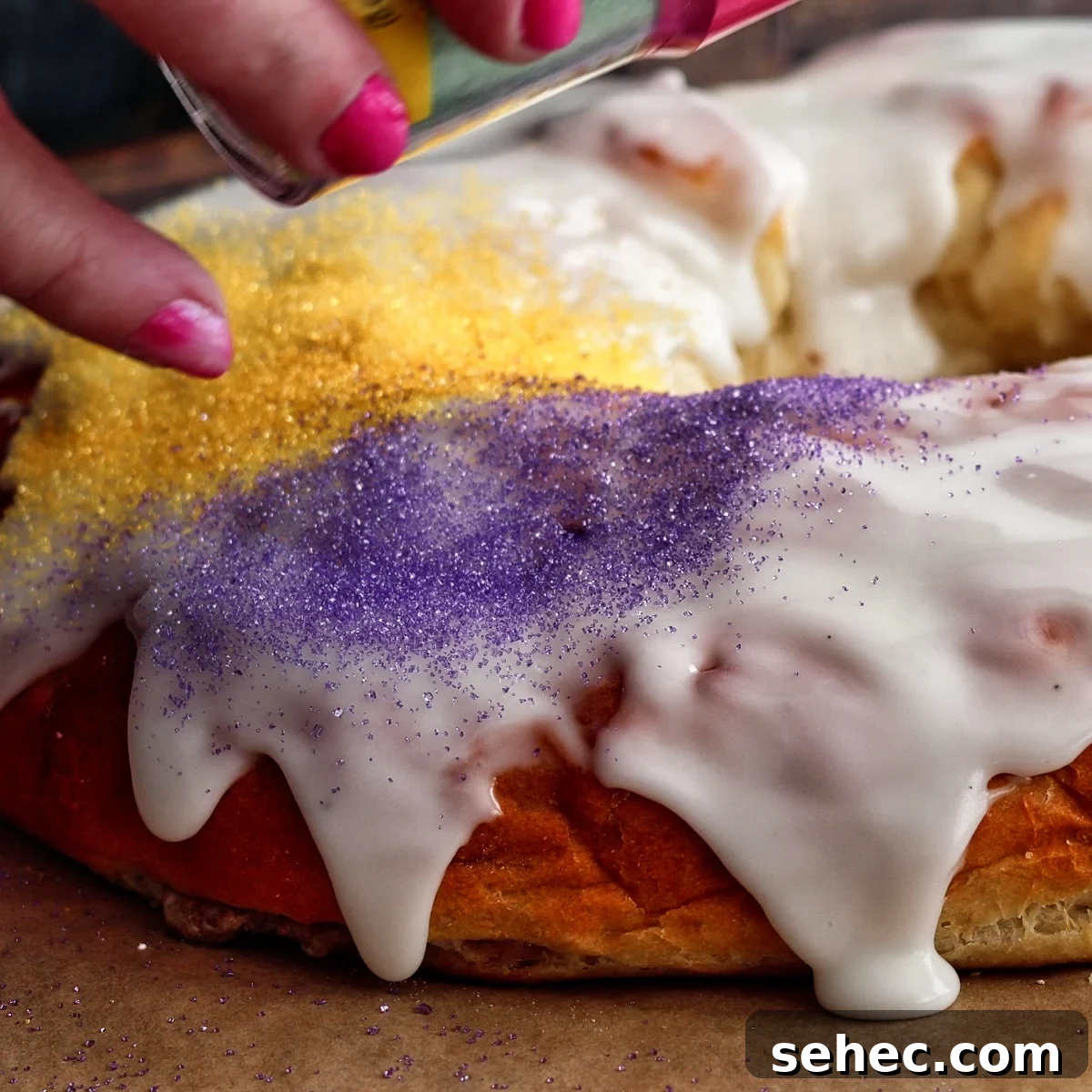 Gluten Free King Cake Recipe for Mardi Gras 17 sprinkling purple, green, and gold colored sugar onto icing on king cake.