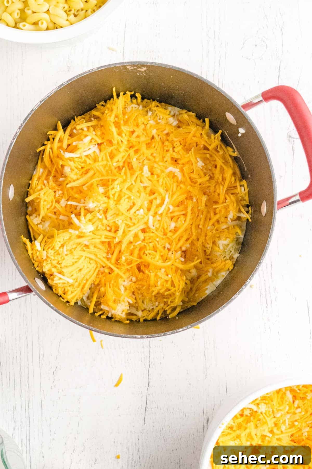 Creamy Eggless Mac and Cheese Recipe 9 A pot with shredded cheese on top of cooked pasta, ready to be mixed.