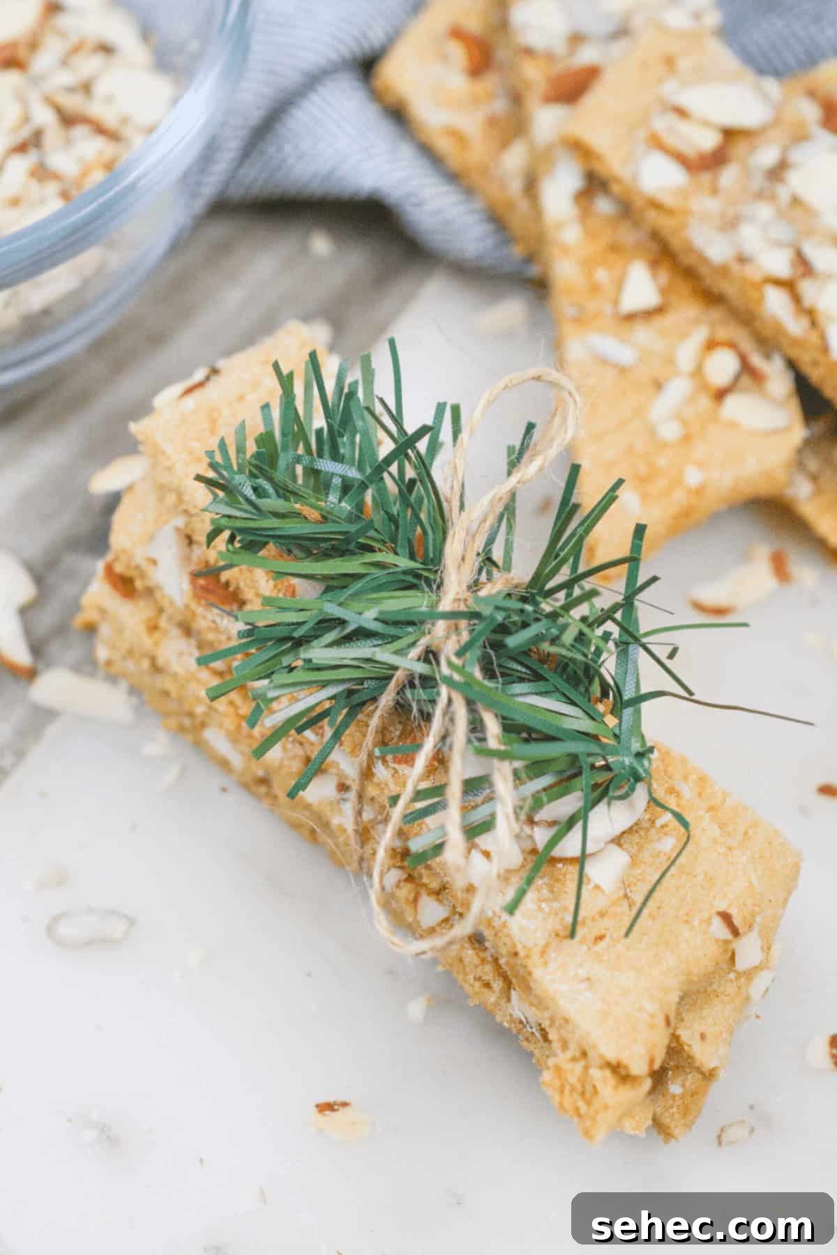 Norwegian Brune Pinner Cookies 3 Dessert are wrapped with twine and adorned with a small pine twig, all elegantly placed on a white surface.