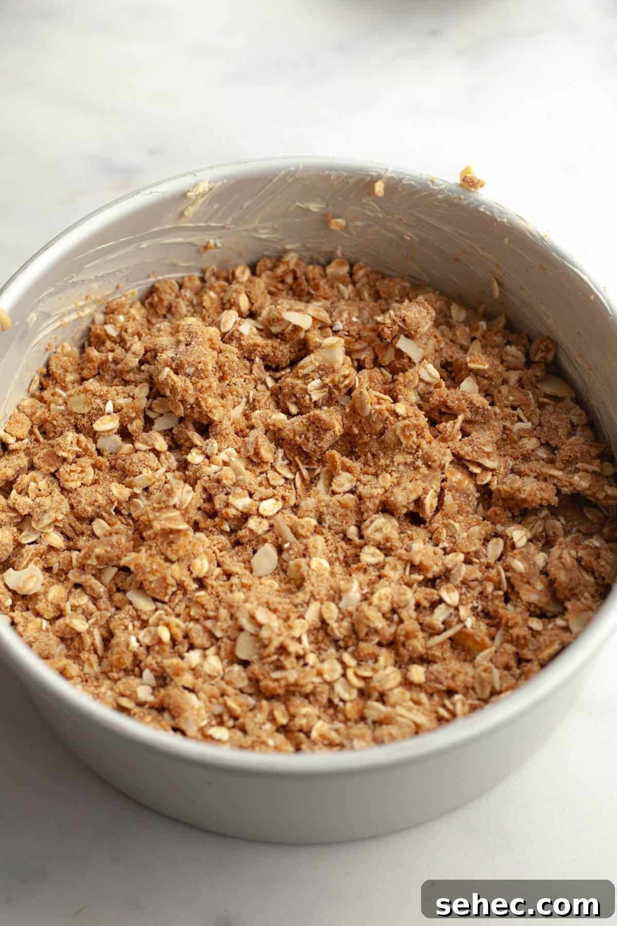 Brown Butter Cardamom Almond Cake Recipe 9 A round cake pan with an unbaked cardamom almond cake covered in an oaty streusel.