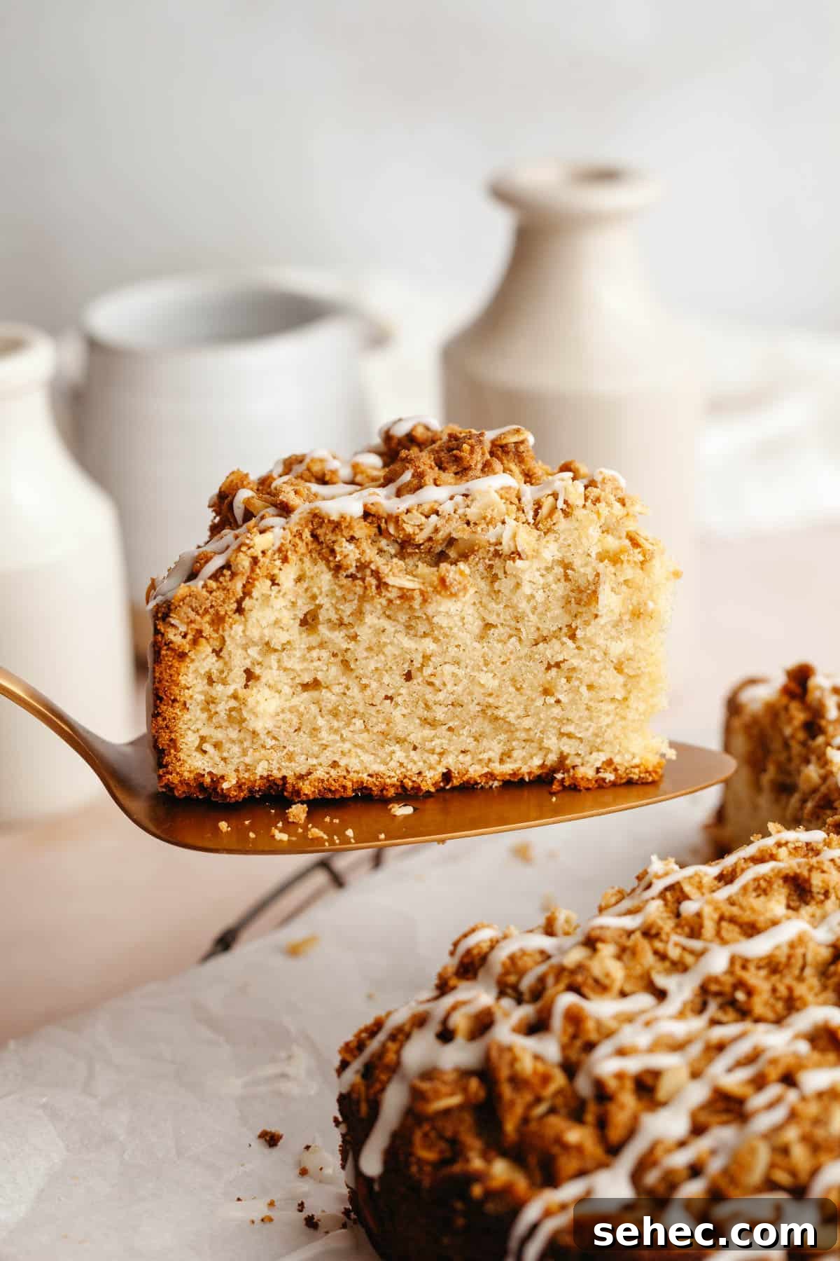 Brown Butter Cardamom Almond Cake Recipe 10 A slice of cardamom almond cake being lifted out with a cake server, drizzled with a glaze.