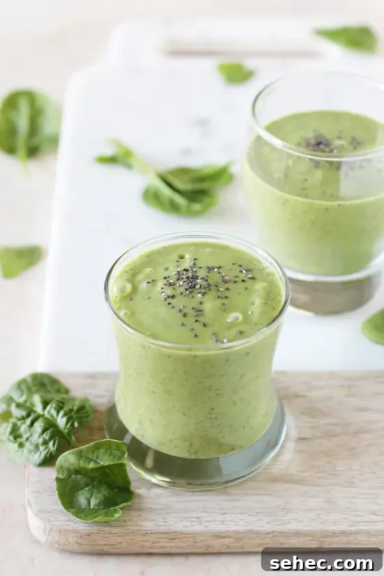 Creamy detox green smoothie with avocado, mango, ginger, cucumber and spinach. Two glasses filled with detox green smoothie set on a cutting board.