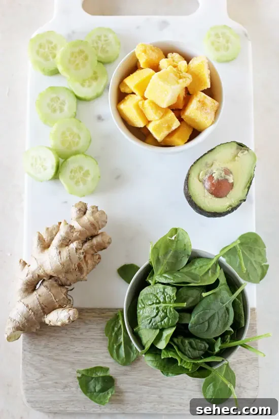 Ingredients for a creamy detox green smoothie with avocado. Diced mango, spinach, cucumber, ginger and avocado on a marble cutting board.