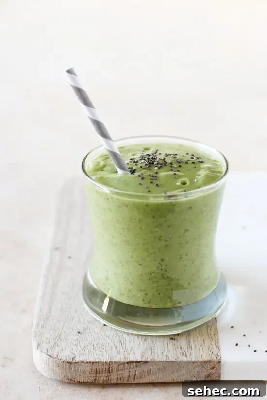 Creamy avocado green smoothie with mango, spinach, cucumber and ginger. A glass filled with avocado green smoothie and a gray straw.