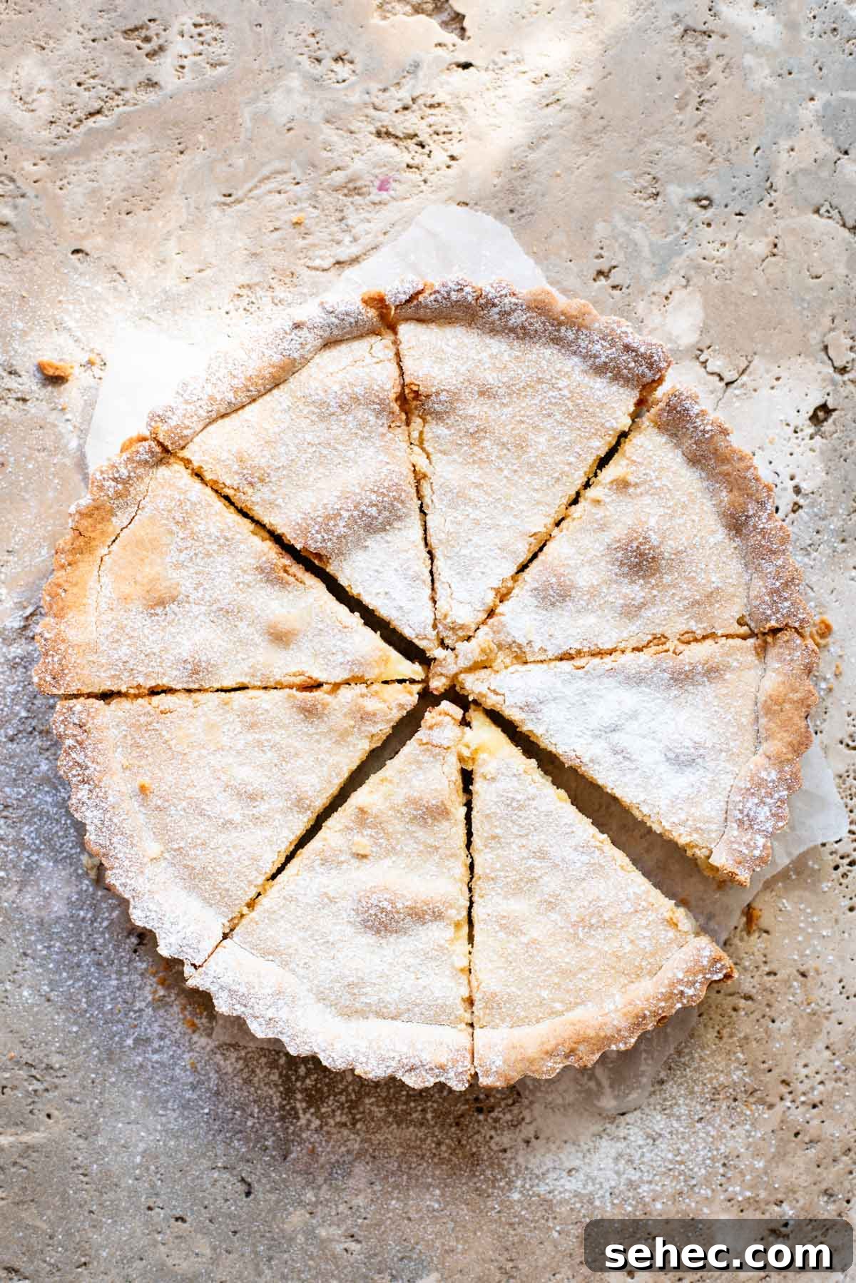 Ricotta and Sour Cherry Crostata 7 A crostata cut into 8 slices and dusted in powdered sugar sitting on a travertine surface.