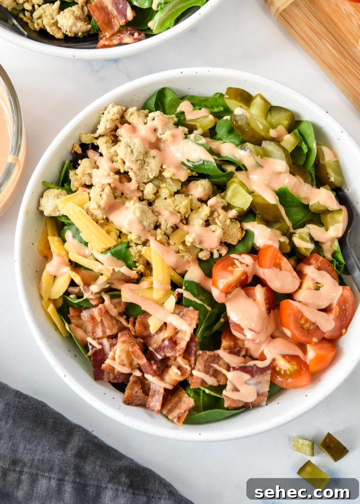 ground turkey burger salad with bacon cheese pickles, serve in a white bowl with special sauce dressing.